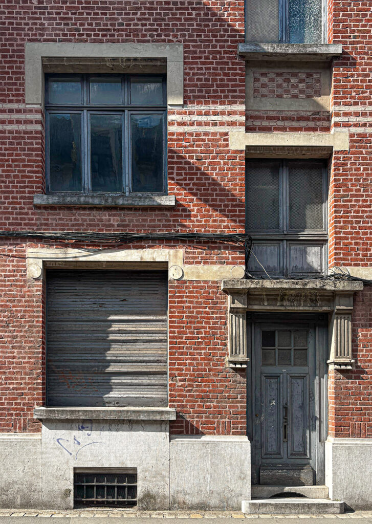 Facade of an old brick bourgeois building with a weathered wooden door, shuttered window, and stone details.