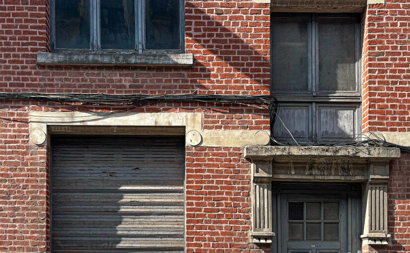 Facade of an old brick bourgeois building with a weathered wooden door, shuttered window, and stone details.