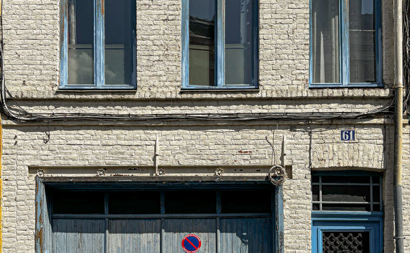 A small white brick house with blue shutters, whose charm still shines through despite the wear.